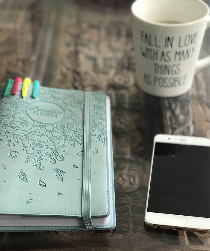 A cell phone, light blue journel and mug sit on a wood table